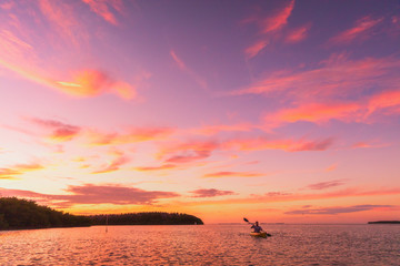 Kayaker man kayaking sea kayak at sunset on summer ocean nature landscape. Amazing scenery with pink colored sky. - obrazy, fototapety, plakaty