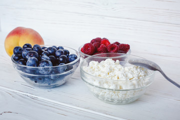 Healthy meal with organic cottage cheese, fresh raspberry, blueberry, peach on white wooden table . close up 