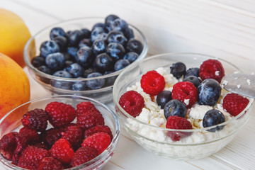 Healthy meal with organic cottage cheese, fresh raspberry, blueberry, peach on white wooden table . close up 