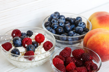 Healthy meal with organic cottage cheese, fresh raspberry, blueberry, peach on white wooden table . close up 