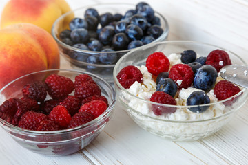 Healthy meal with organic cottage cheese, fresh raspberry, blueberry, peach on white wooden table . close up 