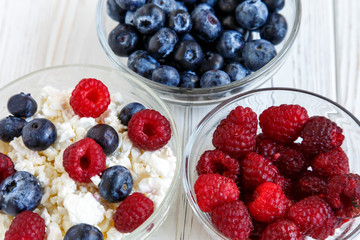 Healthy meal with organic cottage cheese, fresh raspberry, blueberry, peach on white wooden table . close up 