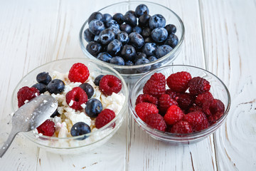 Healthy meal with organic cottage cheese, fresh raspberry, blueberry, peach on white wooden table . close up 