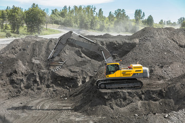 Yellow excavator in career moves overburden. Bulldozer combs the ground, with the bright sun and nice blue sky in the background
