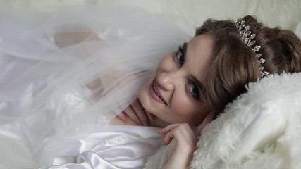 Beautiful and lovely bride in night gown on the bed. Wedding morning. Pretty and well-groomed woman smiling. Slow motion