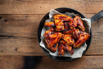 Baked chicken wings in barbecue sauce in a cast iron pan on an old wooden rustic table. Top view...