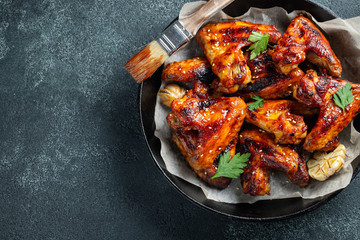 Baked chicken wings in barbecue sauce with sesame seeds and parsley in a cast iron pan on a dark...