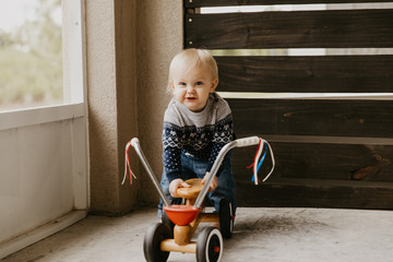 Precious Adorable Cute Little Blonde Baby Toddler Boy Kid Playing Outside on Wooden Toy Bicycle Scooter Mobile Smiling at the Camera and Having Fun