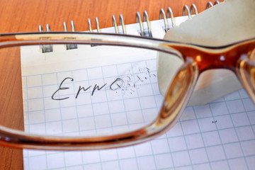 White rubber eraser erases letter of word error written in report on a sheet of Notepad. View through glasses