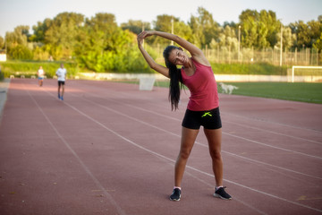 Fototapeta na wymiar one young happy, smiling woman, stretching upper body - arms, leaning to one side. On a stadium, track and field stadium.