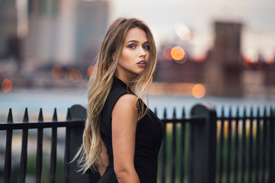 Beautiful woman with long blond hair walking in the city at evening time wearing elegant black dress