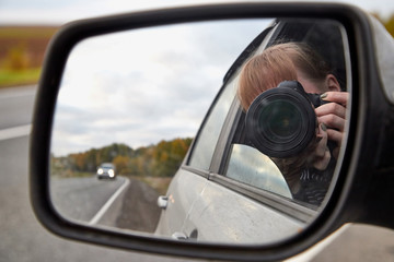 Car mirror, the reflection of the female photographer in it and landscape with field and tree