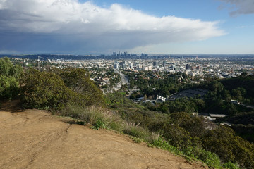 The 101 freeway, Hollywood, and downtown Los Angeles, California are shown in an elevated view from a hiking trail during an afternoon day.