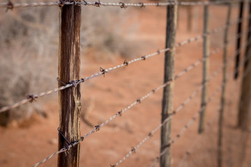 Rusty barb wire fence and old wood poles on Kalahari red sand farm