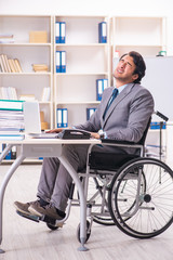 Young handsome employee in wheelchair at the office 