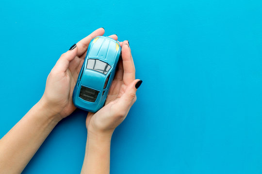 Car insurance concept. Safety of auto. Car toy in female hands on blue background top view copy space