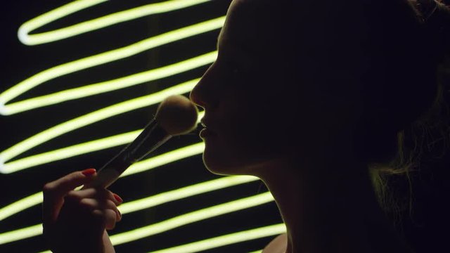 Sequence of videos with female silhouette and her hand holding brush, putting powder on face and then applying lip glosser on lips