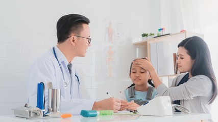 Professional doctor wearing white coat talking to examine kid patient with her mother in hospital background.Concept of disease treatment and health care in hospitals.