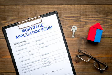 Mortgage concept. Mortgage application form near key and house made of constructor on dark wooden background top view