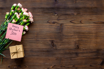 Mother's Day congratulations. Carnations and gift box on dark wooden background top view copy space