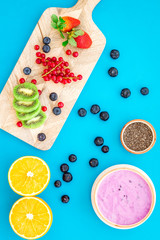 Preparing healthy fruit smoothie. Acai smoothie bowl near cutting board with fresh fruits, berries, chia seeds on blue background top view