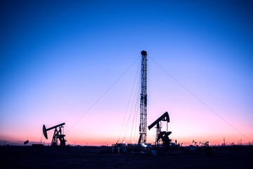 Oil pumps are running in the sunset at the oil field. The outline of the pumping unit.