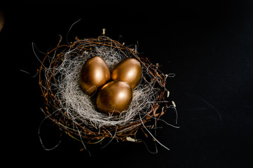 Fototapeta premium Golden Easter Eggs in birds Nest on black background. Easter Holiday concept abstract background copyspace top view several objects.
