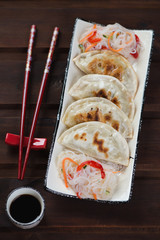 Plate with fried korean potstickers over dark brown wooden background, vertical shot