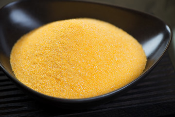 Close-up of raw polenta in a black bowl, selective focus, studio shot