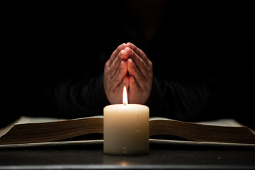 Person Praying with Hands Over Bible Illuminated by Candle Light