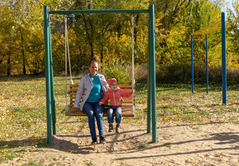 Child with mom ride on a swing in autumn