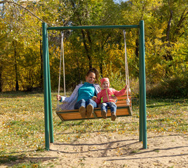 Child with mom ride on a swing in autumn