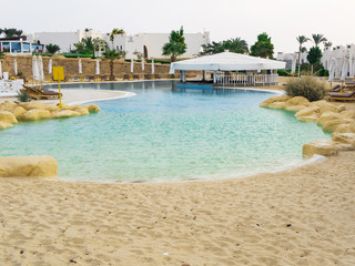 Swimming pool with sand entrance in Egypt. Empty sun-loungers near the pool