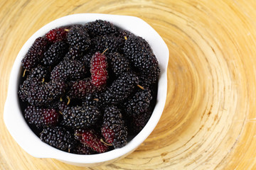 The mulberry fruit in white bowl on wood table.