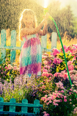 Playfull girl watering flowers with rain in the garden at summer day. Child using garden hose on...