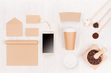 Coffee branding identity mockup - brown paper cup with blank phone,  label, card, notebook, mortar with coffee beans on white wood board, top view.