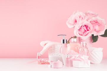 Bath cosmetics products, romantic bouquet and accessories in elegant pastel pink color - massage rose oil, bath salt, cream, soap, perfume, towel on white wood board.