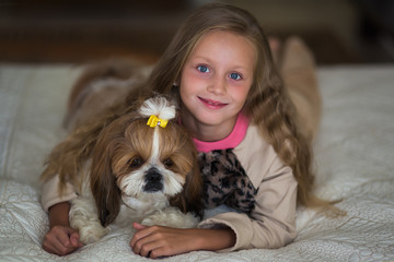 Cute girl with long hair is lying on the sofa with a dog at home.