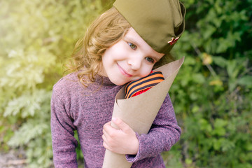 Cute baby girl holding a bouquet of red carnations as a gift to the veteran in honor of the victory in the war on may 9. St. George ribbon - the symbol of the great Victory/Victory Day.