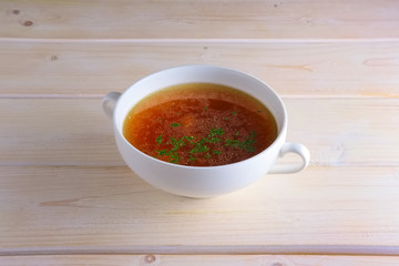 Rich beef broth in small soup bowl Served with fresh dill  on wooden table