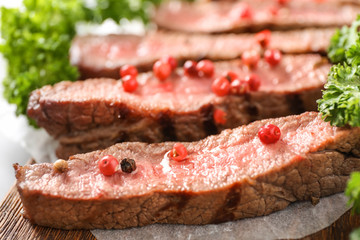 Cut grilled steak with pink pepper on wooden board, closeup