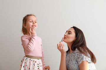 Portrait of cute little girl and mother with lipsticks on light background