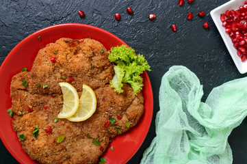 Large Viennese schnitzel on a red plate with lemon on a black background. Meat dish. Top view, flat...
