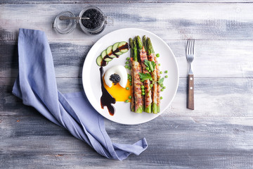Plate with bacon wrapped asparagus and egg on wooden table