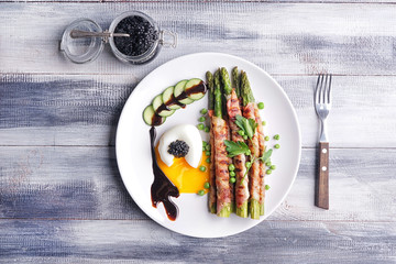 Plate with bacon wrapped asparagus and egg on wooden table