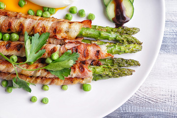 Plate with bacon wrapped asparagus on wooden table, closeup