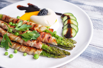 Plate with bacon wrapped asparagus on wooden table, closeup