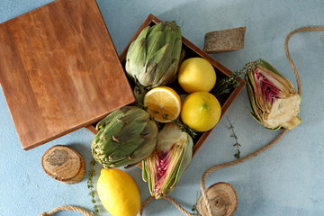 Wooden box with tasty raw artichokes and lemon on table