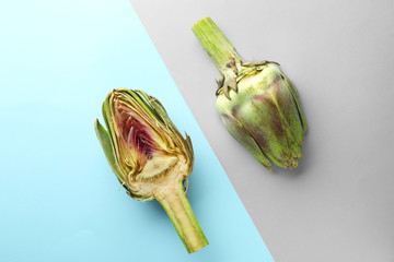 Halves of tasty raw artichokes on color background