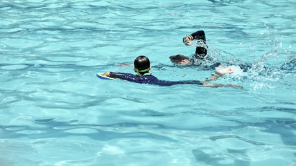 Child practicing flutter kick with kick board and looking teacher show swimming at the pool  : Swimming lesson